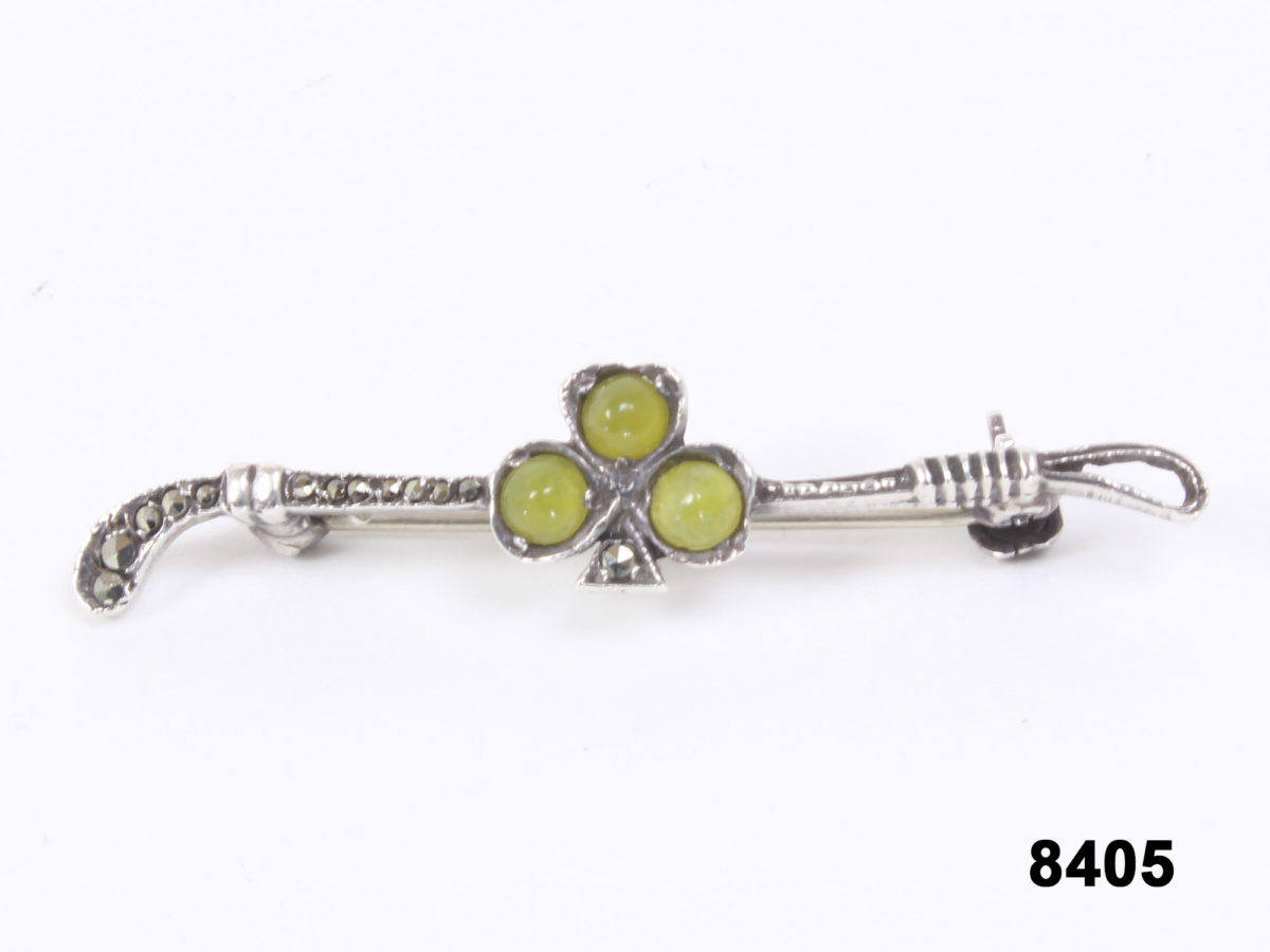 Front view of Silver marcasite bar brooch in the form of a horse racing whip with a shamrock of 3 green stones in the centre from Antiques of Kingston.