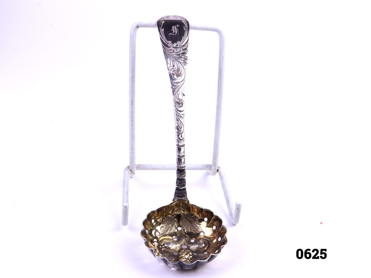 Antique silver strainer spoon with gilt bowl decorated with fruit Traditionally used to strain fruit especially berries c1829 London assayed Bowl measures 43mm in diameter and 13mm deep Photo of front of spoon from raised angle showing full length of spoon and gilt bowl interior