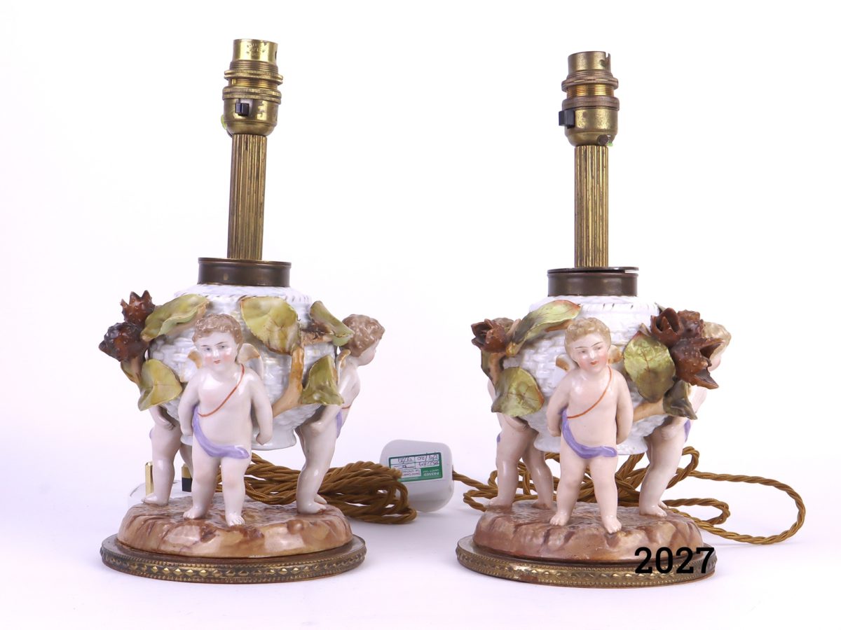 Antique pair of Continental porcelain lamps decorated with 3 winged cherubs holding a basket with leaves & beech nut seed pods Measures 140mm in diameter at base Main photo showing the pair of lamps