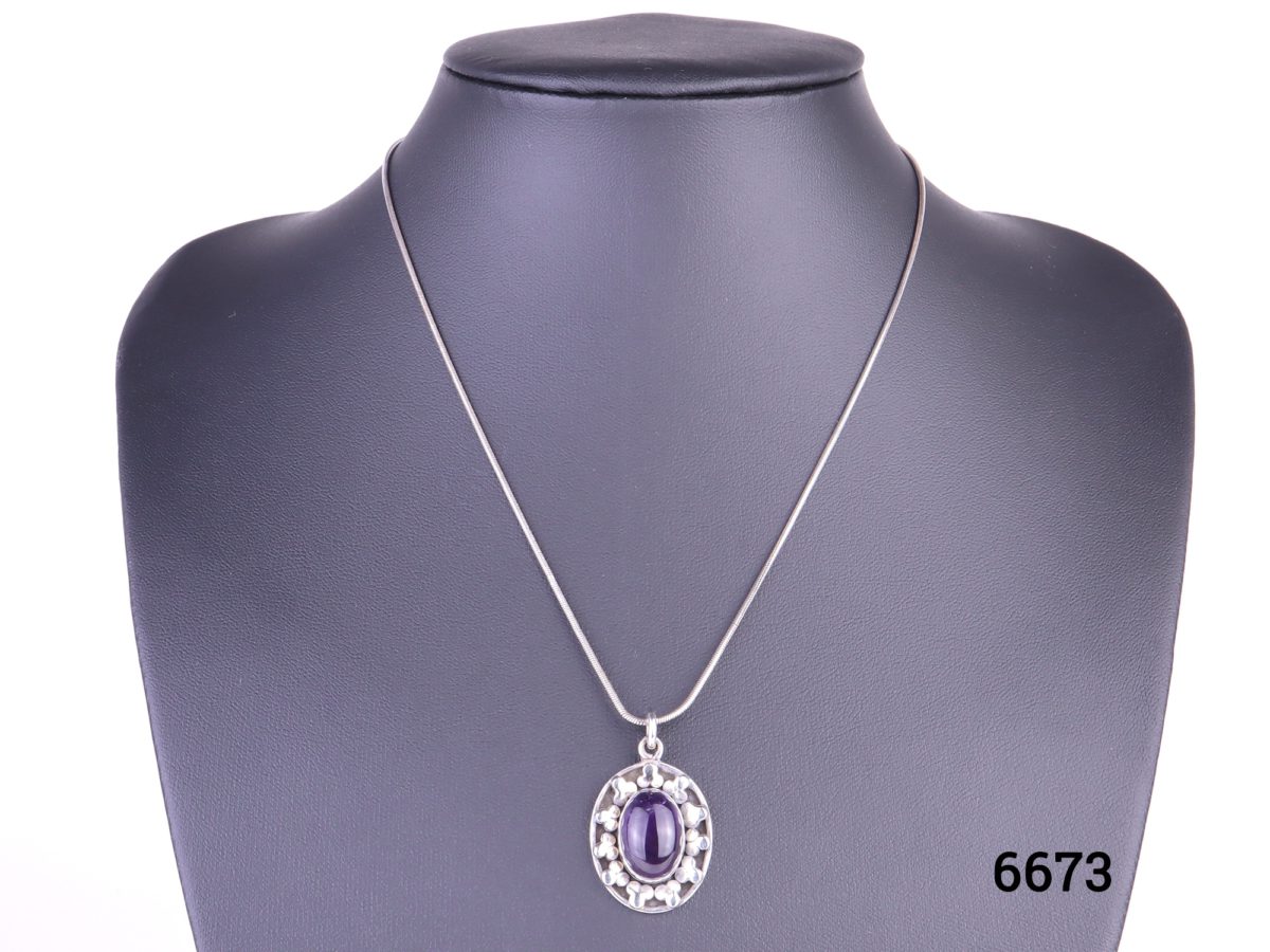 925 Sterling silver and amethyst cabochon pendant on a sterling silver snake chain Pendant drop length 32mm and Chain measures 405mm long. Weight 9.4g. Main photo of necklace displayed on a stand.