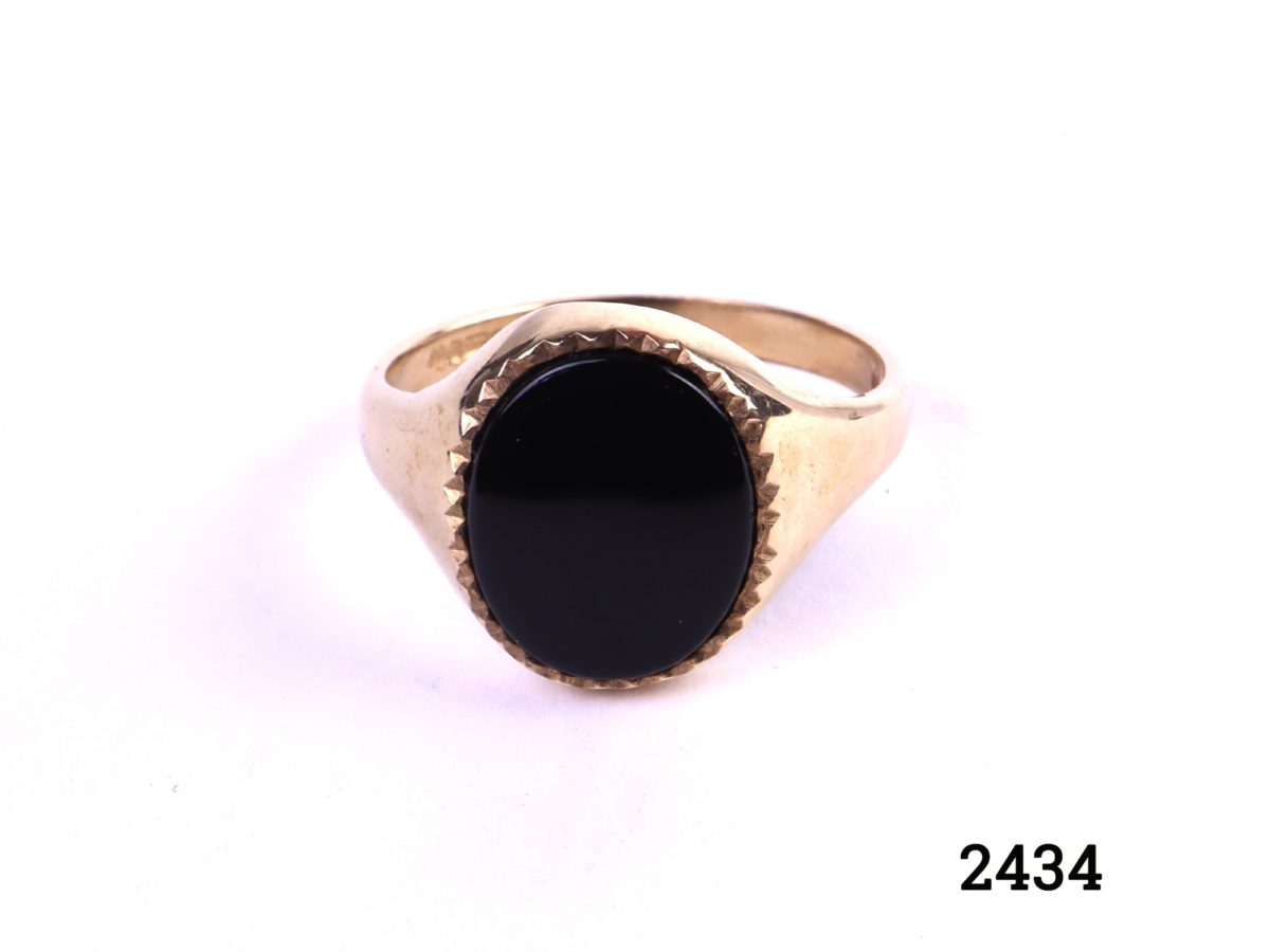 9ct Gold signet ring with black onyx c1988 Birmingham assayed fully hallmarked 375 and makers stamp AK Stone size 12mm by 10mm Size P / 7.5 Image of ring on flat surface showing onyx front