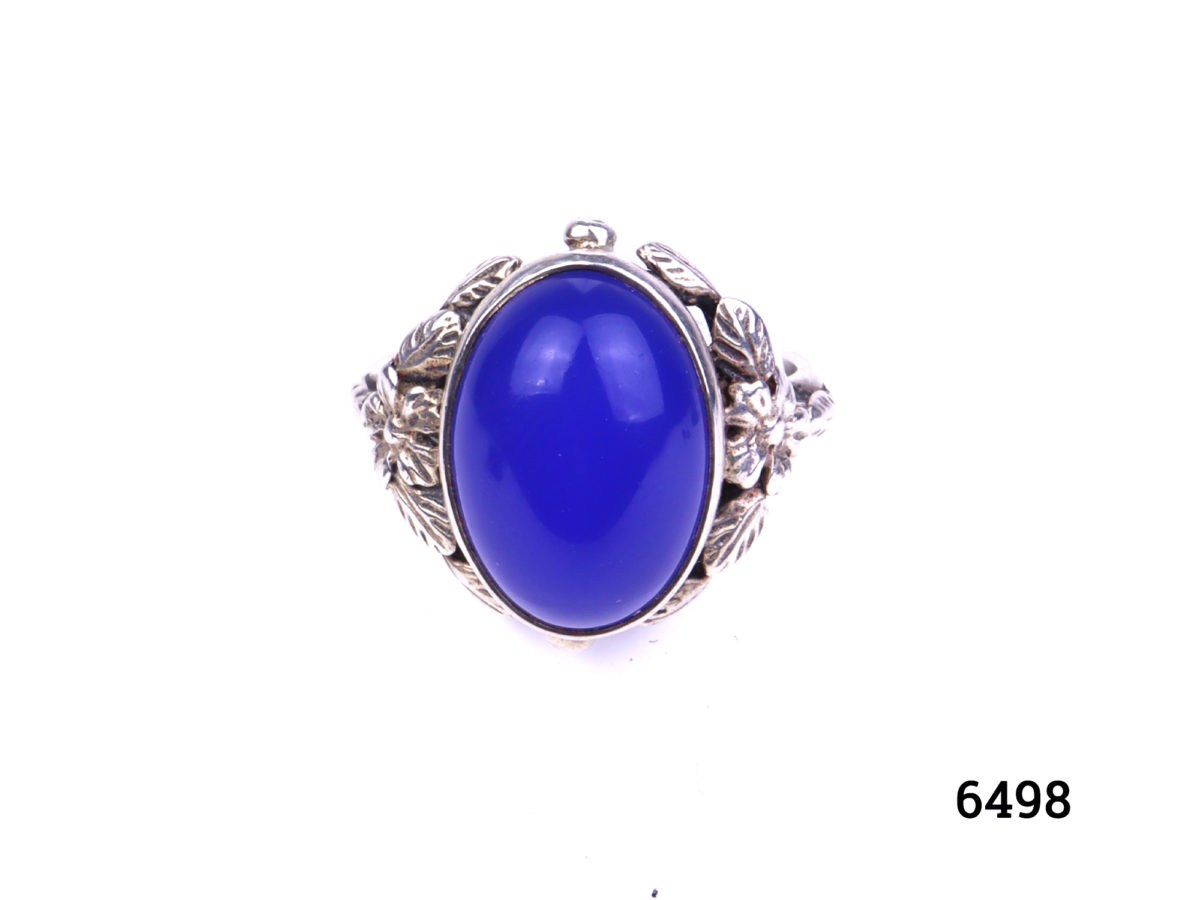 Arts & Crafts ring by Bernard Instone. Hallmarked silver ring set with bright sea blue oval chalcedony stone to centre and floral motifs to the shoulder either side. Size N / 6.5. Main photo showing ring on display stand front view.