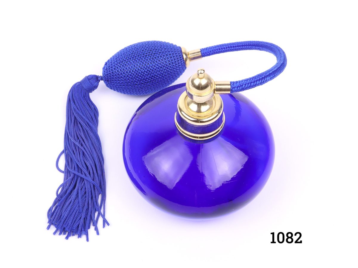 Modern cobalt blue glass perfume bottle with atomiser in matching cobalt blue with tassels. Measures 90mm in diameter Photo looking down at perfume bottle and atomiser from above