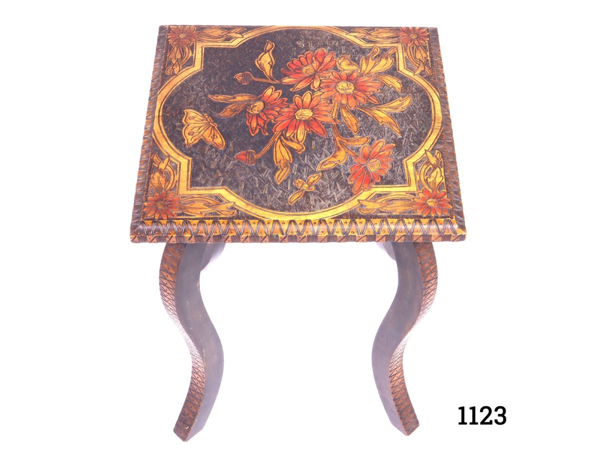 Small vintage pokerwork table stained red and decorated with flowers, butterflies and bees. (Pokerwork is a method of decorating wood by burning a design into it.) Top measures 305mm square Photo looking down on the table showing the decorated pokerwork top