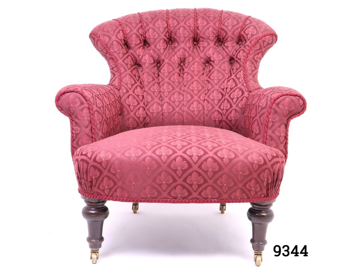 Vintage low armchair in burgundy fleur-de-lis style patterned fabric with button back back rest and wooden legs with brass castors Measures 780mm arm to arm width, 700mm back width and 560mm cushion depth Main photo showing chair from the front