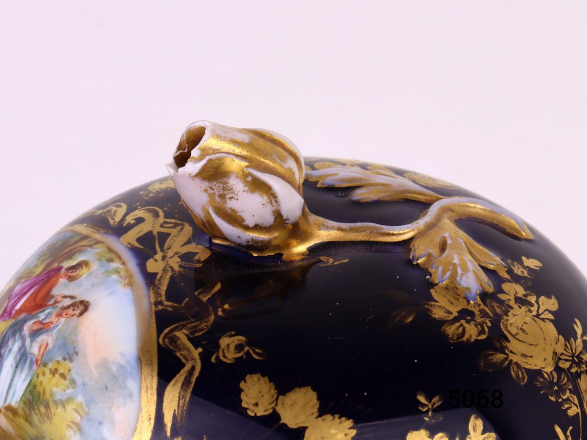 Antique Meissen small lidded bowl in royal blue with gilt throughout and decorated with intricate hand-painted images of courting couples. Rose bud to top of lid intact with minor chips at the edges and some gilt wear. Measures 45mm ín diameter at base and 80mm across the top.     Base of lid measures 86mm Close up of the rose bud handle on top of lid showing gilt wear
