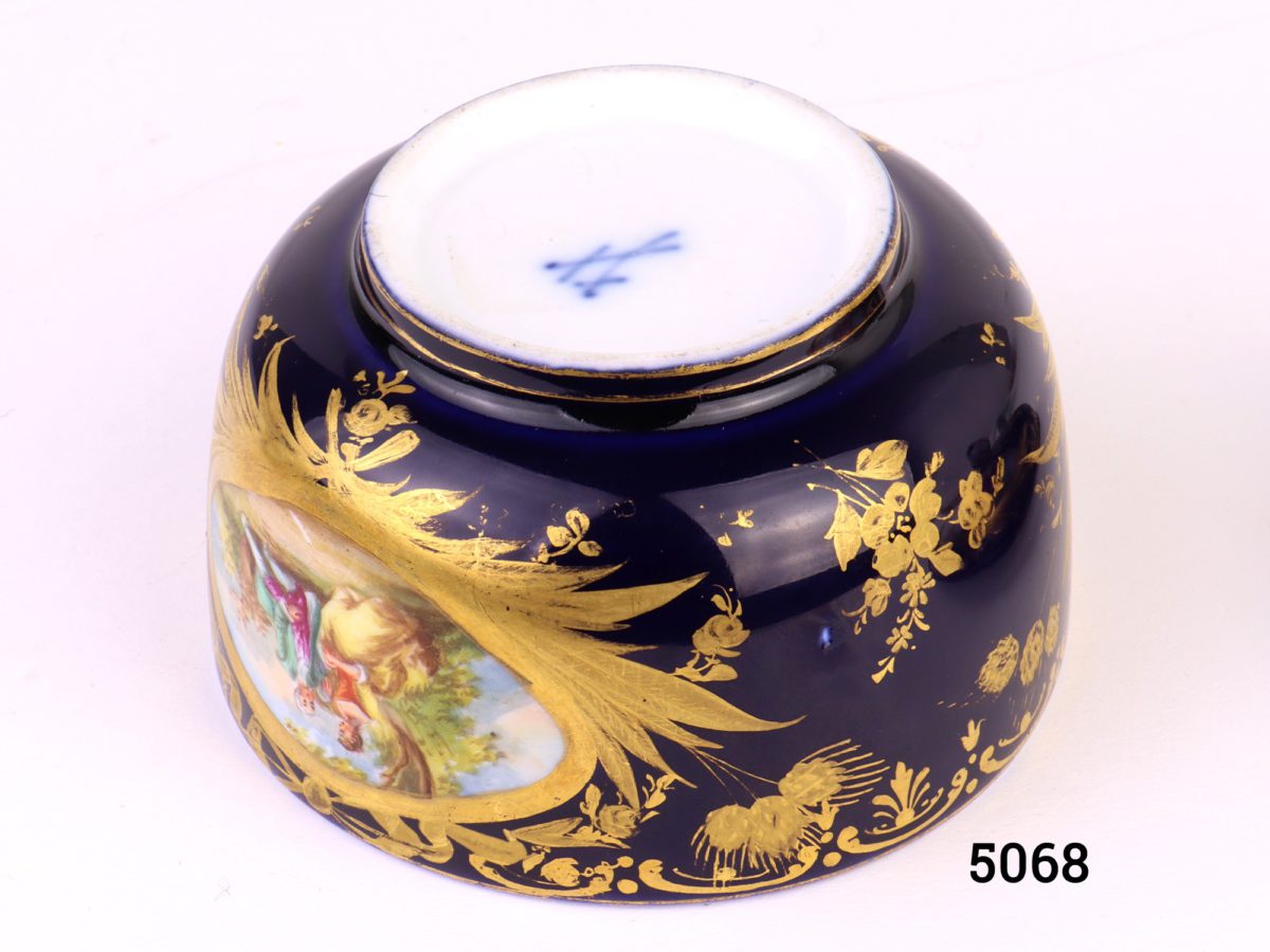 Antique Meissen small lidded bowl in royal blue with gilt throughout and decorated with intricate hand-painted images of courting couples. Rose bud to top of lid intact with minor chips at the edges and some gilt wear. Measures 45mm ín diameter at base and 80mm across the top.     Base of lid measures 86mm Close up photo of the makers mark on the base