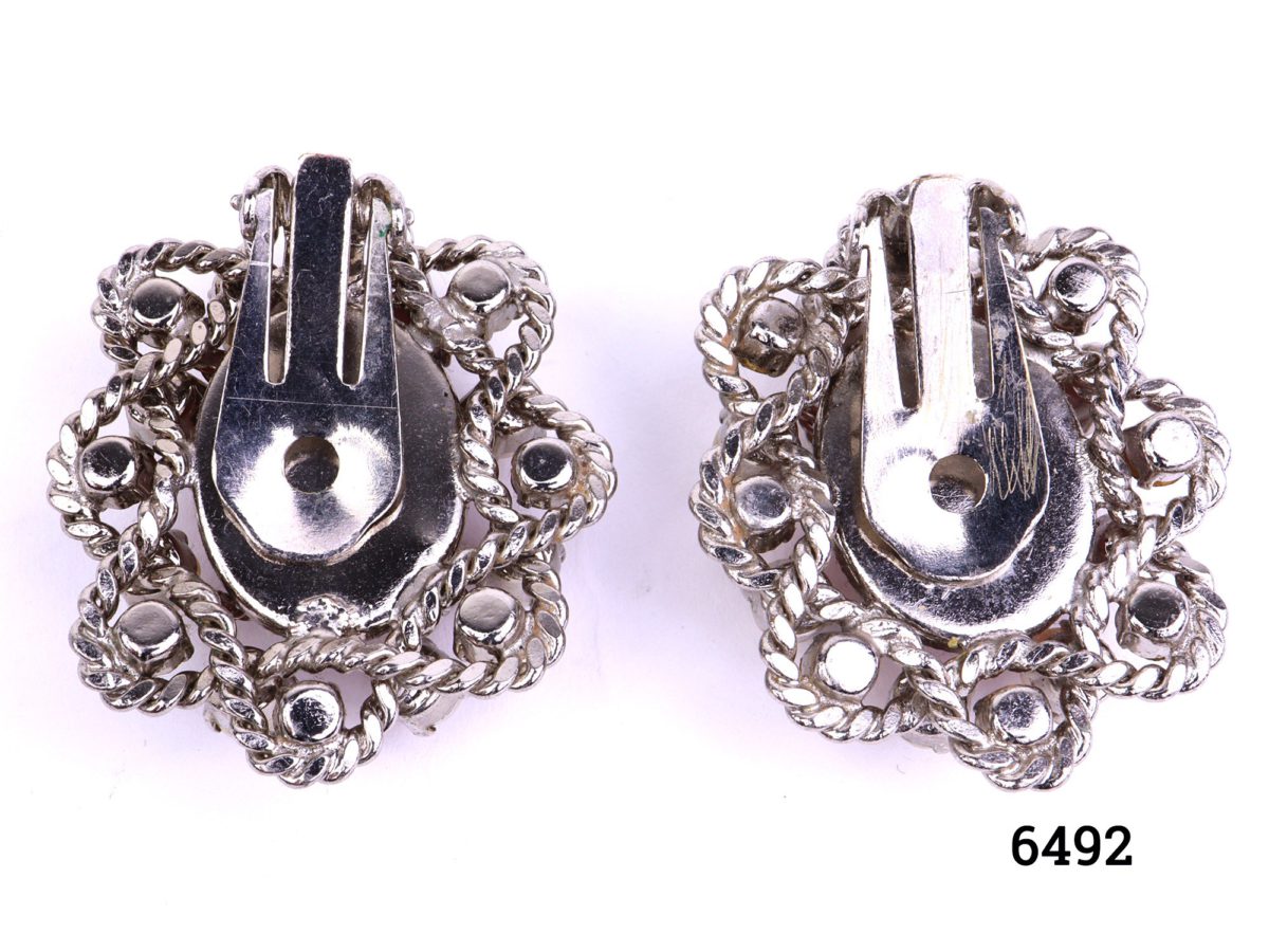 Vintage clip-on earrings with pink glass stone centre decorated with faux pearls and glass stones set on silver coloured metal. Measures 35mm by 30mm Both clips in good order Photo showing the back clips side of earrings