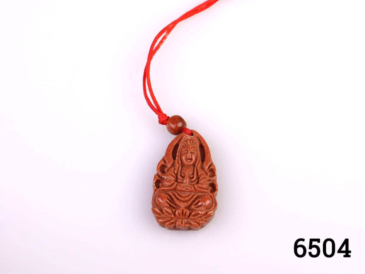 Vintage carved goldstone charm pendant of Guan Yin (The Buddhist Bodhisattva of compassion) Strung on customary red string Charm measures 32mm long by 20mm wide Close up photo of the charm
