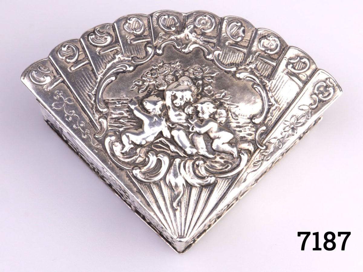 Antique Continental silver fan shaped box decorated with Cherubs to the lid and natural scene on the sides. Hallmarked 800 for Continental silver to the base and makers stamp (part worn) Measures 98mm at widest point and 74mm deep Photo of top of box lid showing the cherub decoration