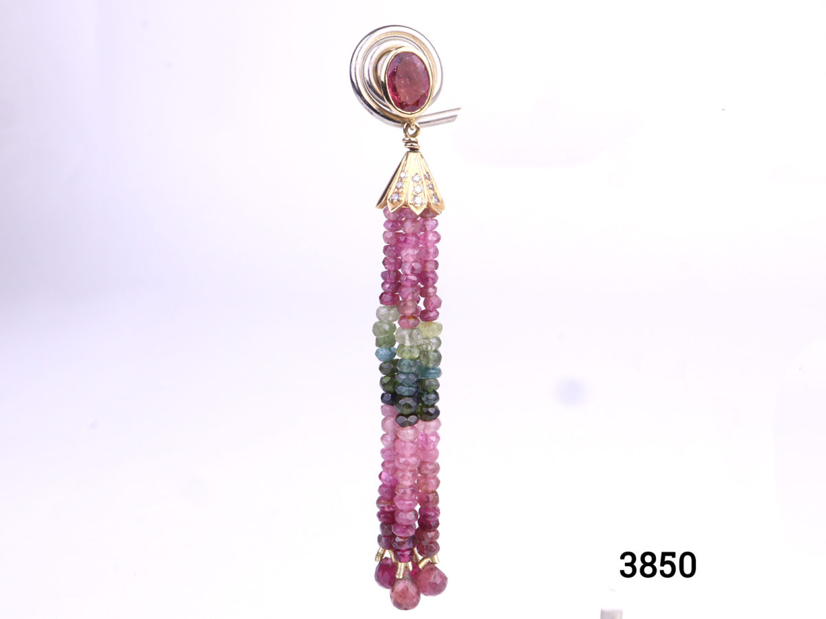 18k gold earrings with tourmaline in graduated shades of pink and green with diamonds in the top housing cover. Drop length 70mm Photo of one earring displayed on a stand