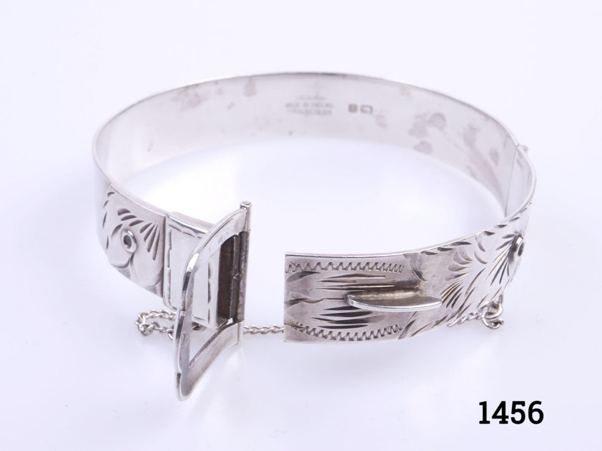 c1978 Birmingham assayed vintage sterling silver bracelet. Solid silver bracelet in popular 70s buckle design. Made by Excalibur jewellery Ltd. Open gap measures 50mm wide. Closed bangle measures approximately 60mm in diameter. Width at buckle 20mm. Photo of bracelet with buckle opening area open and sshowing safety chain