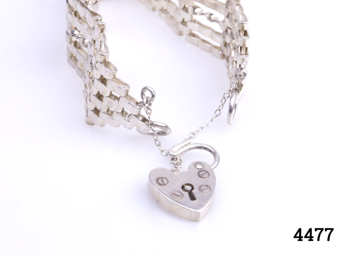 Birmingham assayed sterling silver 5 bar gate bracelet with heart shaped padlock and safety chain. Made by Henry Griffith and Sons. Measures 110mm when fully open. Photo of bracelet on flat surface focusing on open heart lock and safety chain