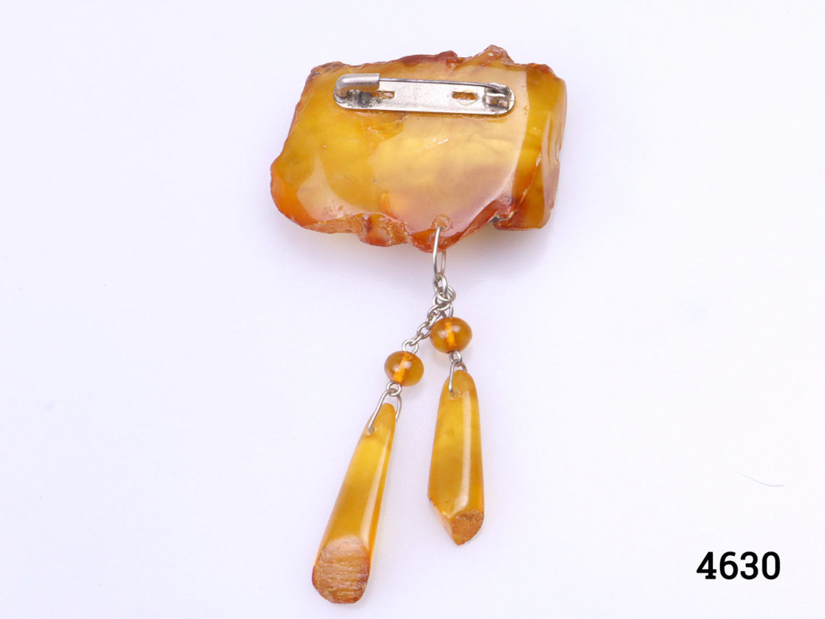 Large antique amber piece up-cycled into a brooch with 2 hanging amber droplets. White metal clasp. Brooch weighs 12grams. Drop length including hanging amber droplets 80mm. Large antique amber piece measures 45mm by30mm. Photo of back of brooch with amber droplets straight down as it would hang