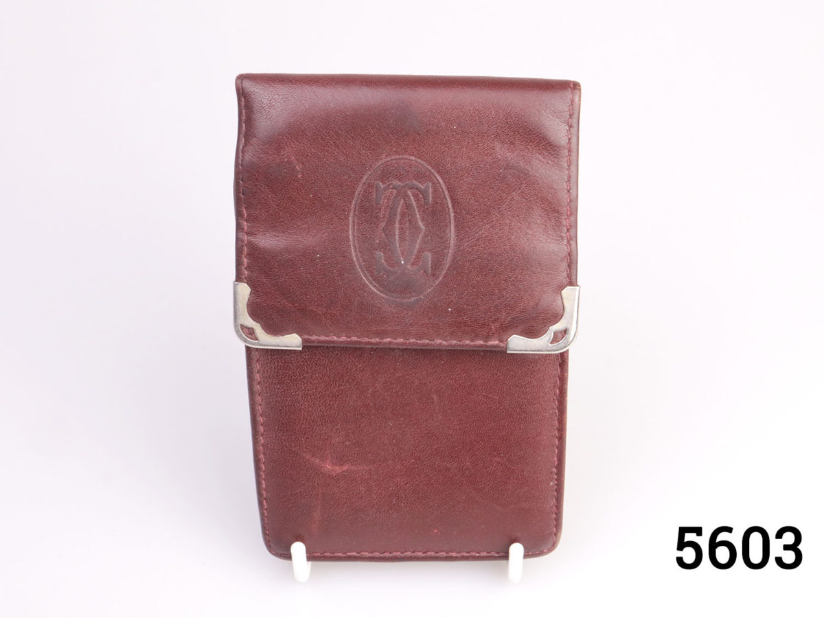 Vintage fine leather Cartier cigarette pouch in a rich maroon tan colour. White metal corner guards on each opening tab corner and famous Cartier logo embossed in the centre to the tab. (Very useful as a card holder) Photo of closed case displayed on a stand and seen from the front