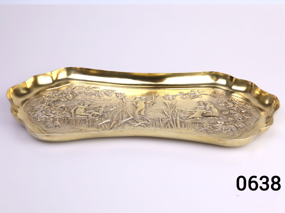 c1901 London assayed gilt silver oblong dish. Decorated with embossed scene of a family playing by the river bank with reeds and brambles. Fully hallmarked for sterling silver and made by William Comyns & Sons Photo of dish on a flat surface from a slight raised angle