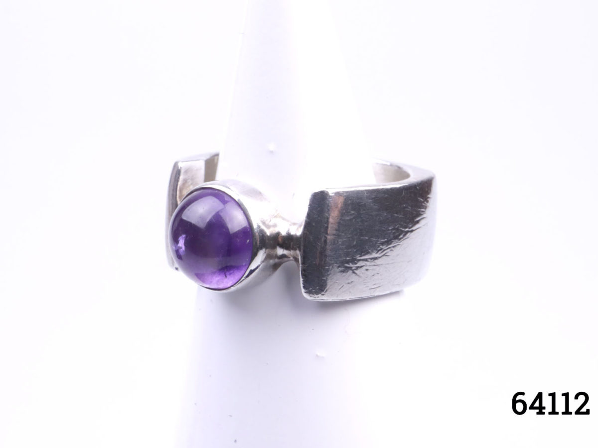 c1974 Peter Guy Watson ring. Modernist sterling silver ring with unusual square cut band and amethyst stone to the centre. Band width 10mm. Ring size Q / 8 Ring weight 12.6grams Photo of ring on display stand from a side angle