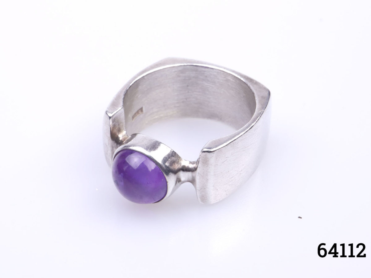 c1974 Peter Guy Watson ring. Modernist sterling silver ring with unusual square cut band and amethyst stone to the centre. Band width 10mm. Ring size Q / 8 Ring weight 12.6grams Photo of ring on flat surface from a raised slightly angled view