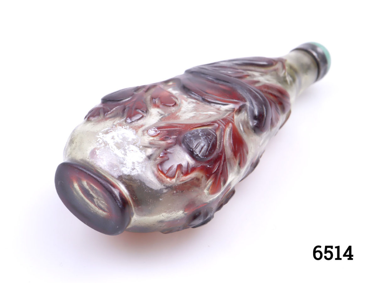 19th Century Peking glass snuff bottle. Teadrop shaped clear glass bottle with red floral overlay and green glass topped spoon. Photo of bottle laid flat with base in the foreground to the bottom left
