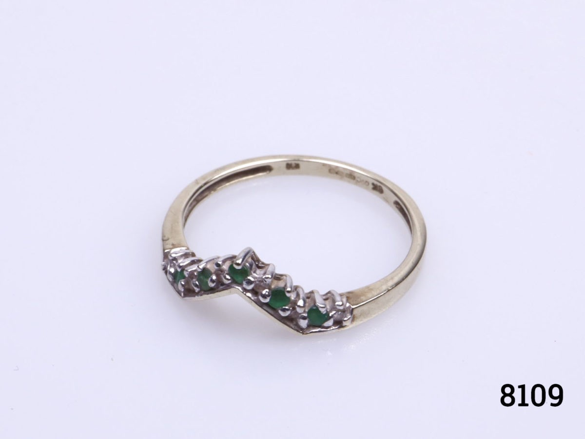 Vintage 9 karat gold ring. Wishbone shape to the front and set with 5 small emeralds and 6 small diamonds. Size P.5 / 7.75. Ring weight 1.9 Photo of ring on a flat surface from a slight side angle