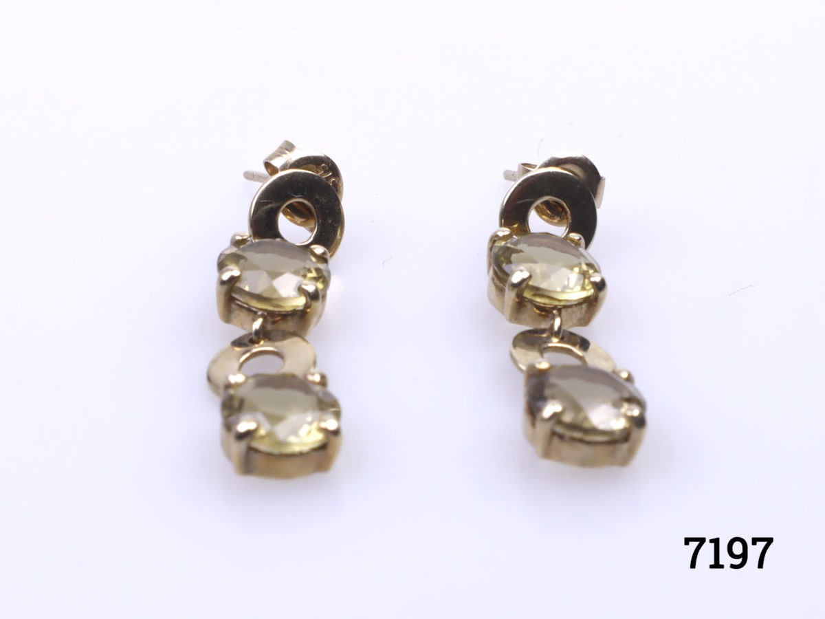 Vintage 9 karat gold earrings set with 2 round cut citrines to each. Drop length 28mm. Earrings weigh 3.6grammes Close up photo of both earrings displayed on a flat surface