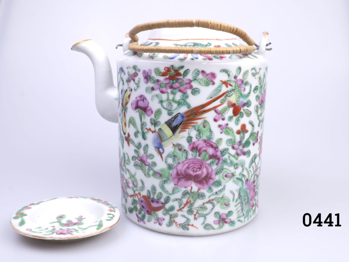 Antique Famille Rose teapot. Hand-decorated in a floral scene with birds and butterflies. (The spout tip has had a professional repair). Measures 130mm in diameter at base and 210mm tall with handle extended. Photo of teapot shown from a side angle with spout to the left. Lid removed and placed below the spout.