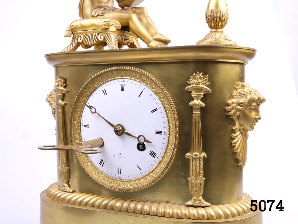 Antique French clock c1810s. Heavy clock in gilt ormolu from the first French empire. Fine detail decoration with an angel reading by firelight. Back cover missing. Key included. Fully serviced and guaranteed for 1 year. Photo of main clock part seen from a slight side angle with key in one slot