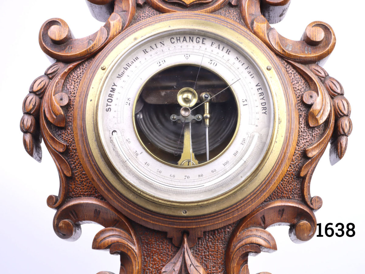 Small antique Victorian barometer and thermometer. Intricately carved solid oak with shield crest at the top. Fully serviced and guaranteed for 1 year from date of purchase. Close up photo of the barometer face with thermometer integrated in the lower area of face