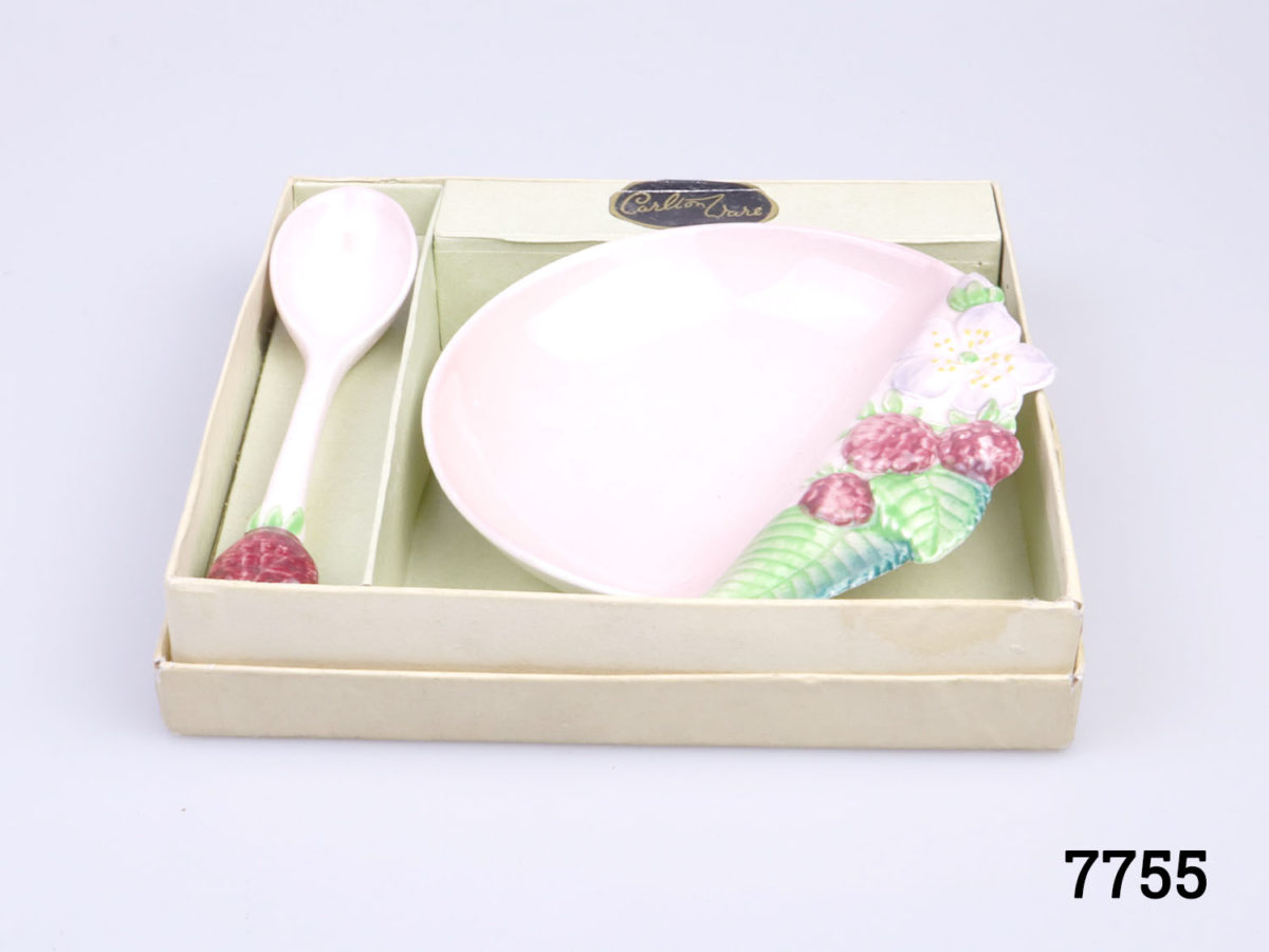 Vintage 1930s preserve set. Small raspberry preserve dish in raspberry pink decorated with raspberry fruit, flower and leaves and matching spoon with raspberry to tip of handle. Slight discolouration at tip of spoon bowl. Box has some signs of wear. Dish measures 112mm long by 110mm wide and 25mm deep. Spoon measures 120mm long. Photo of spoon and dish set in place inside the gift shown from a raised anglebox