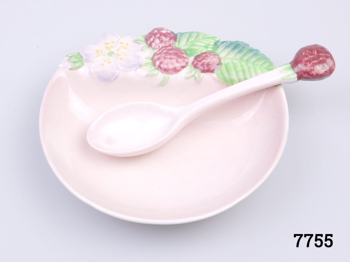 Vintage 1930s preserve set. Small raspberry preserve dish in raspberry pink decorated with raspberry fruit, flower and leaves and matching spoon with raspberry to tip of handle. Slight discolouration at tip of spoon bowl. Box has some signs of wear. Dish measures 112mm long by 110mm wide and 25mm deep. Spoon measures 120mm long. Photo of spoon placed in the dish as seen from above looking in