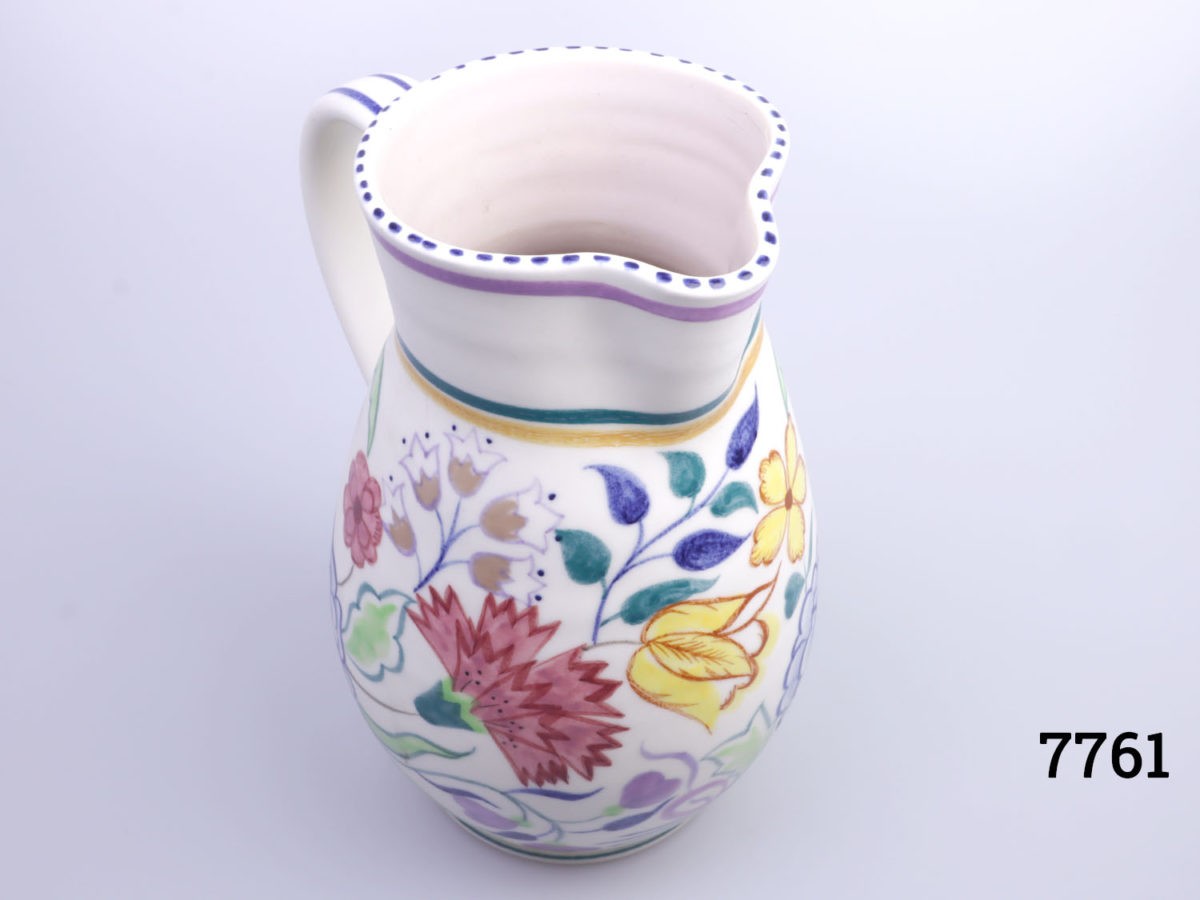 Vintage medium sized Poole Pottery jug. Hand decorated with multi-coloured flowers on a cream background with cream interior. Measures 85mm in diameter at base Photo of jug seen diagonally and from a slightly raised angle with spout facing bottom right