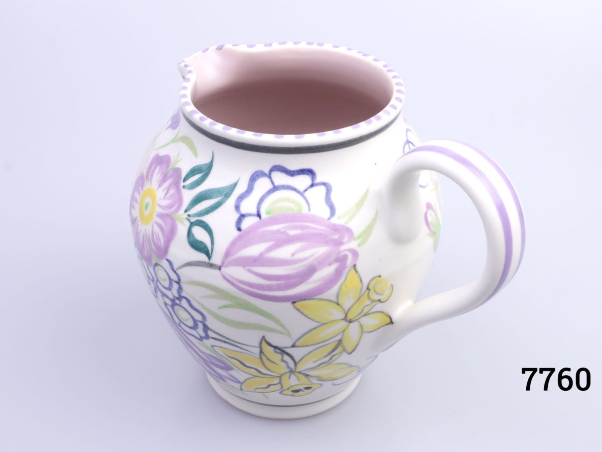 Vintage small Poole Pottery jug with spring flowers in lilac, green and yellow with pale pink interior. (Tiny chip to the lip). Measures 60mm in diameter at base. Photo of jug from a slightly raised angle peering slightly inside at the pale pink interior