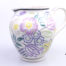 Vintage small Poole Pottery jug with spring flowers in lilac, green and yellow with pale pink interior. (Tiny chip to the lip). Measures 60mm in diameter at base. Main photo showing jug from euye level with handle to the right
