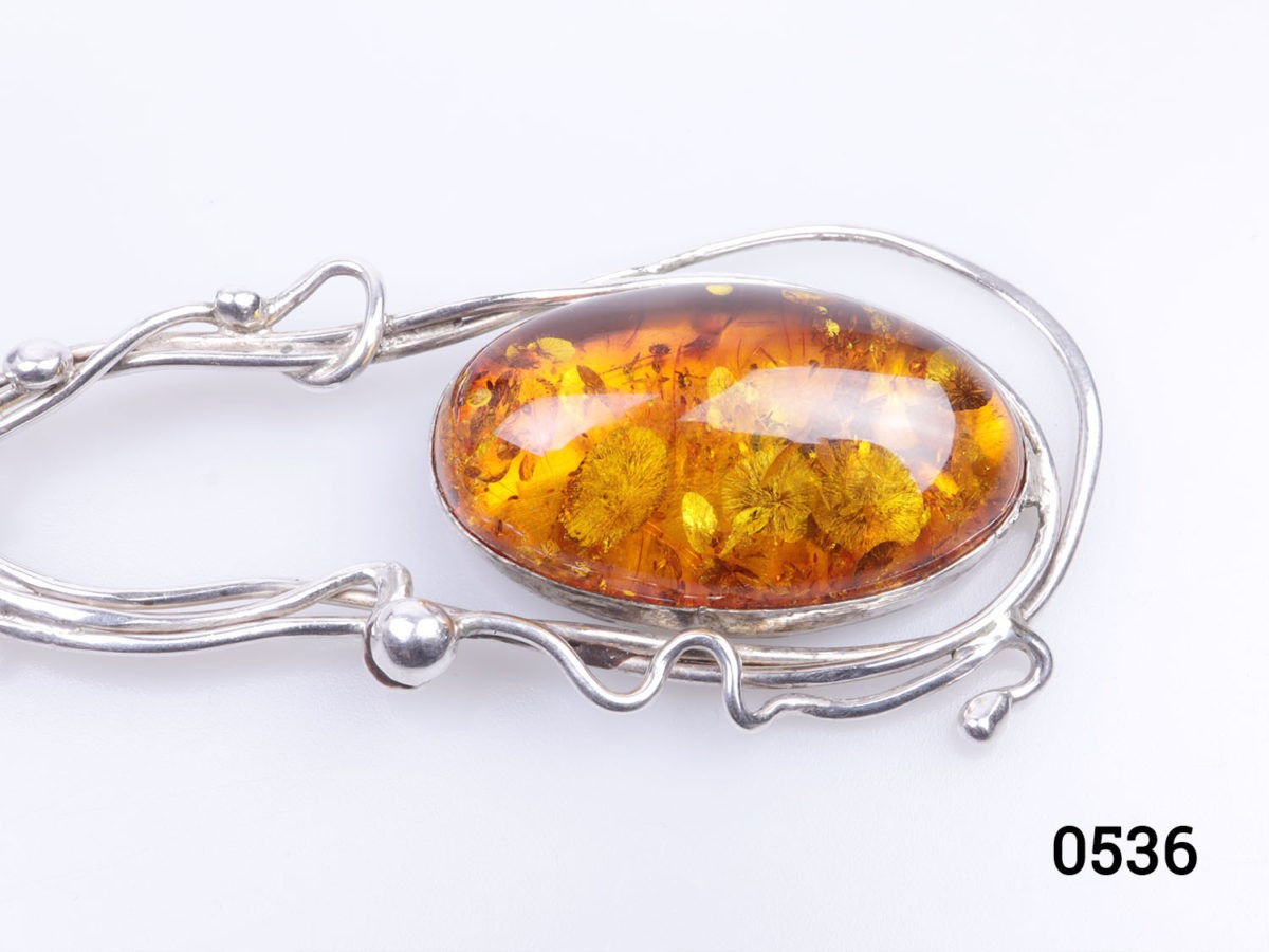 c1990s Vintage sterling silver pendant with large amber cabochon. Amber set on sterling silver in an eclectic design mix of modernist and Art Nouveau styles. Fully hallmarked for London assay. Measures 40mm at widest point. Drop length 115mm from bail to bottom of pendant. Close up photo of the amber cabochon
