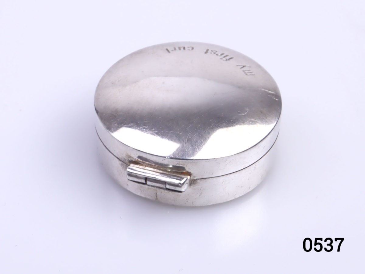 c1990s vintage small sterling silver circular box inscribed "My First Curl" Fully hallmarked to the base for London assay. Measures 30mm in diameter. Photo of box with hinge part in the foreground