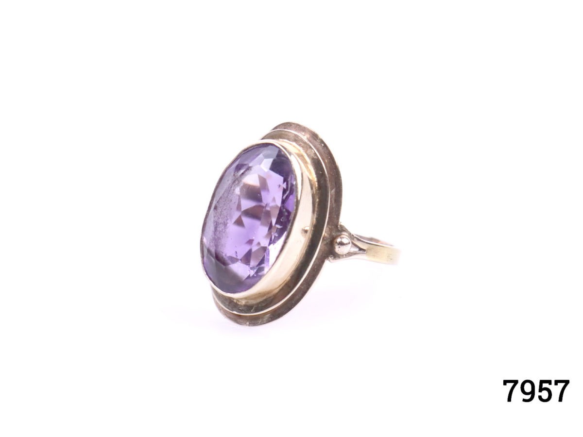 Rose gold dress ring with oval cut amethyst. Worn hallmark on outer band of ring at back. Ring front measures 23mm by 12mm. Ring size Q / 8. Photo of ring on a flat surface seen from a slight side angle