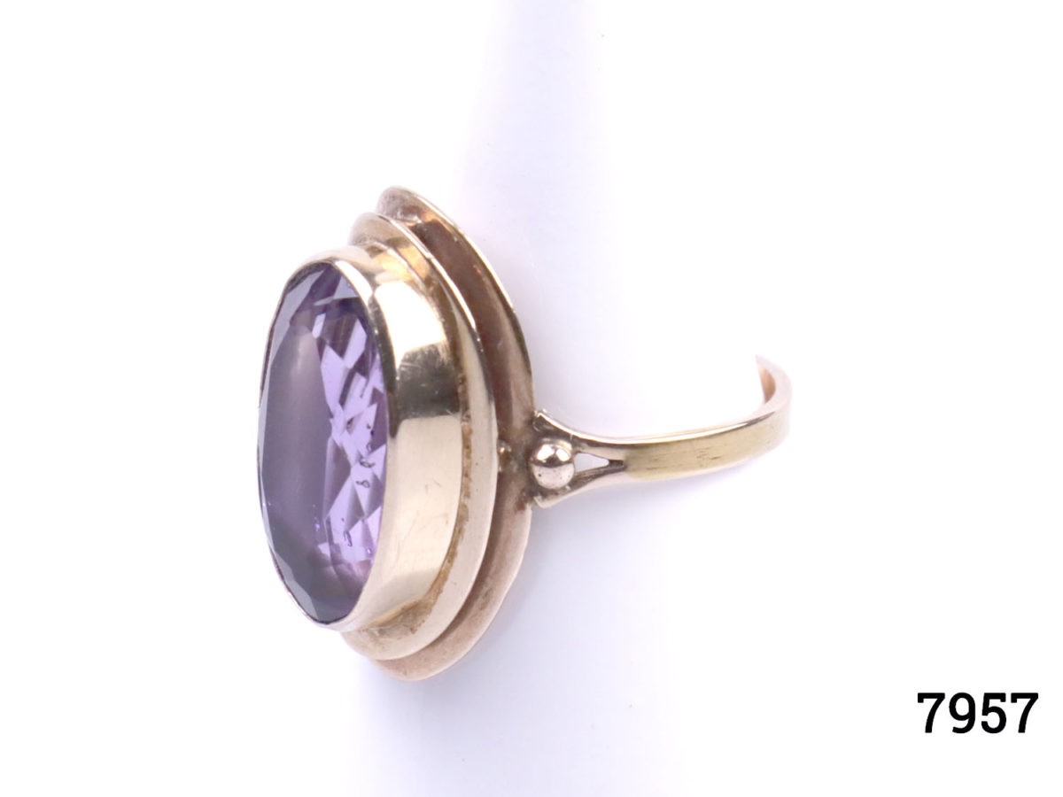 Rose gold dress ring with oval cut amethyst. Worn hallmark on outer band of ring at back. Ring front measures 23mm by 12mm. Ring size Q / 8. Photo of ring on display stand seen from a slight side angle