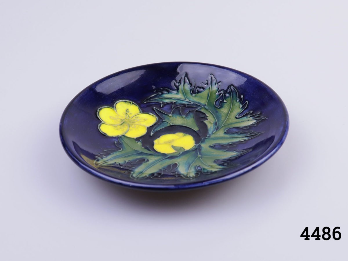 Small Moorcroft pin dish in cobalt blue with buttercup design. Measures 120mm in diameter. Photo of dish on a flat surface slight angle looking down