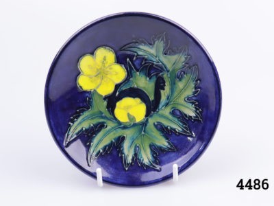 Small Moorcroft pin dish in cobalt blue with buttercup design. Measures 120mm in diameter. Main photo of dish on a display stand