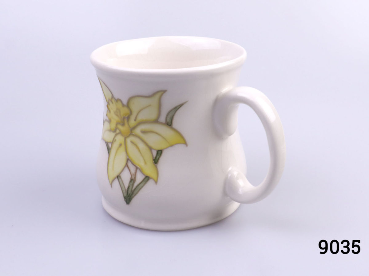 Vintage Moorcroft mug in daffodil pattern. Impressed Moorcroft mark to the base. c1980s. Measures 80mm in diameter at base Photo of mug at a slight diagonal angle with handle to the bottom right corner