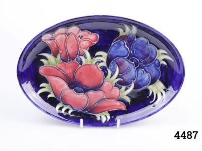 Vintage Moorcroft oval plate in cobalt blue anemone design with dark pink and blue anemone flowers. Pattern 1930. Main photo of dish displayed on a stand and seen straight on from the front
