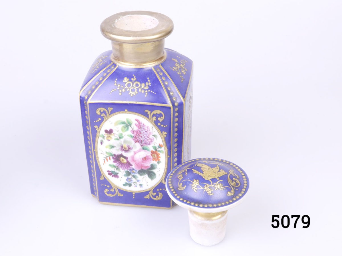 Antique pair of Paris porcelain perfume bottles. Cobalt blue porcelain bottles each decorated with hand-painted floral images and finished in gilt throughout. Some wear to gilt on both bottles. Each bottle measures 75mm by 75mm and 170mm tall. Photo of one bottle with lid removed and placed to the right side of bottle looking slightly down from above.