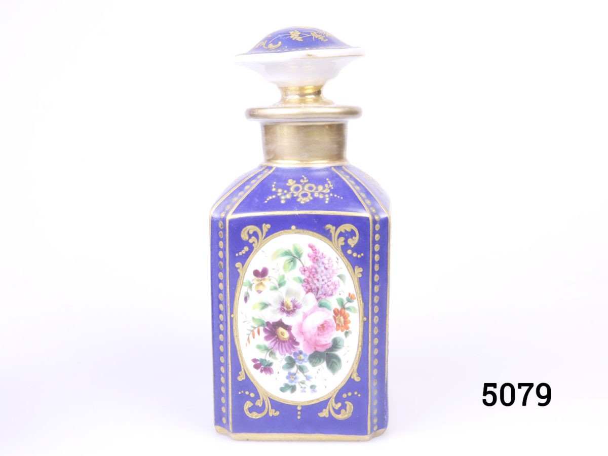 Antique pair of Paris porcelain perfume bottles. Cobalt blue porcelain bottles each decorated with hand-painted floral images and finished in gilt throughout. Some wear to gilt on both bottles. Each bottle measures 75mm by 75mm and 170mm tall. Photo of one bottle shown with floral image in the foreground