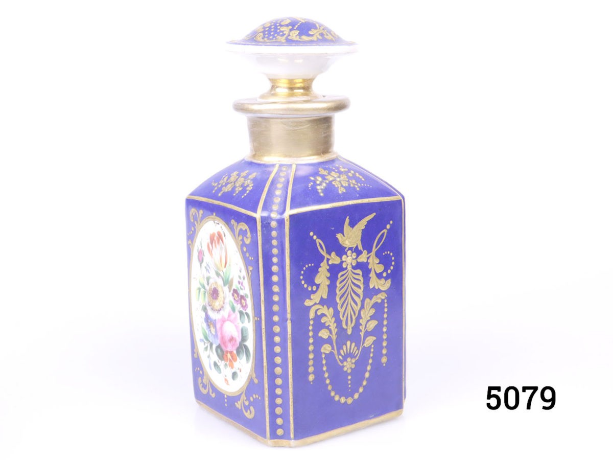 Antique pair of Paris porcelain perfume bottles. Cobalt blue porcelain bottles each decorated with hand-painted floral images and finished in gilt throughout. Some wear to gilt on both bottles. Each bottle measures 75mm by 75mm and 170mm tall. Photo of one bottle shown from a slight angle with corner edge in foreground