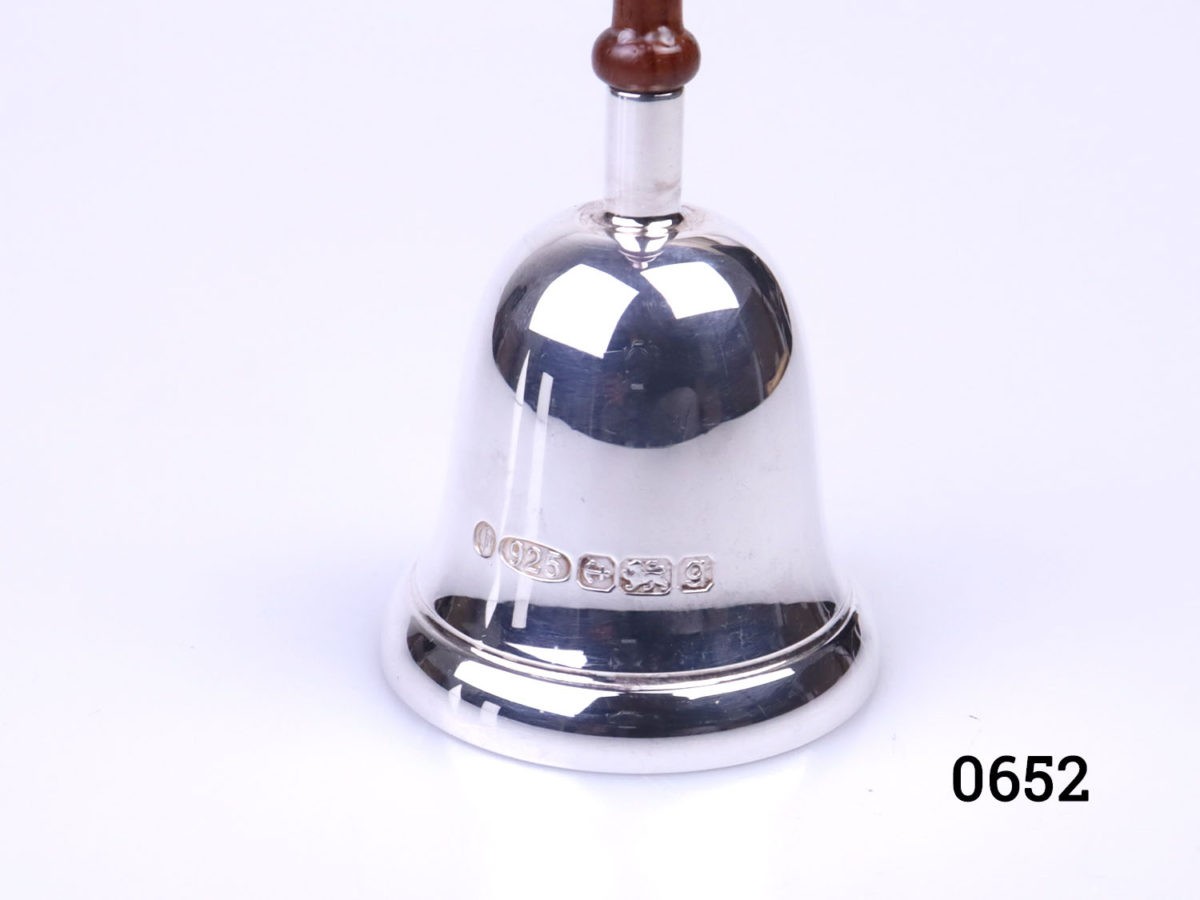 Small sterling silver hand bell with wooden handle. Fully hallmarked to the side of the bell for Birmingham assay and made by L. J. Millington c 2006. Bell measures 46mm in diameter Close up photo of the hallmark on the side of the bell