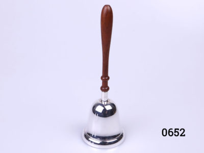 Small sterling silver hand bell with wooden handle. Fully hallmarked to the side of the bell for Birmingham assay and made by L. J. Millington c 2006. Bell measures 46mm in diameter Main photo of whole hand bell seen from a near eye level angle