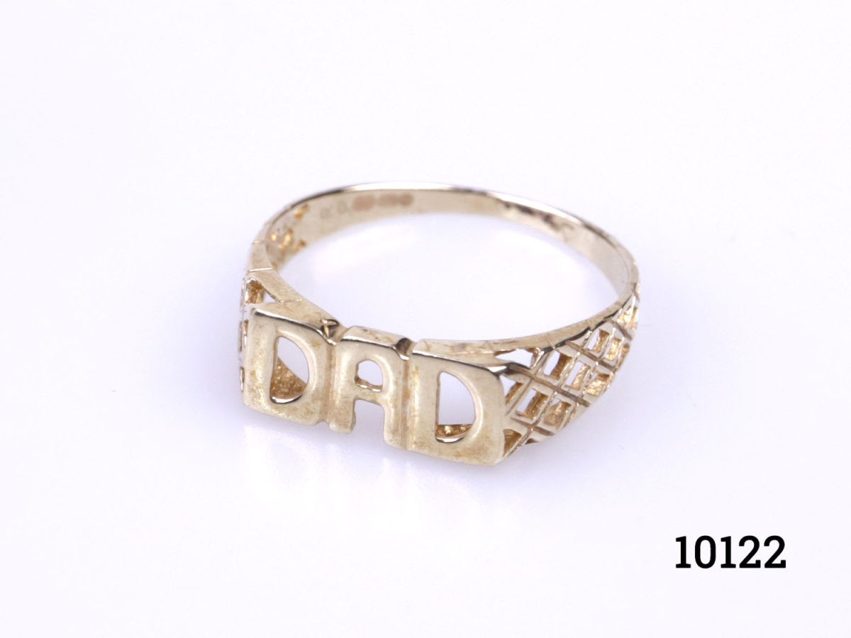 Vintage 9 karat gold "DAD" ring. Ring with Dad spelt out at front with nice lattice work to the shoulders. Hallmarked 375 for 9 karat gold. Ring size R / 8.5 and weight 1.7grams (Band is very fine at the back) Photo of ring on a flat surface and set at a slight diagonal angle