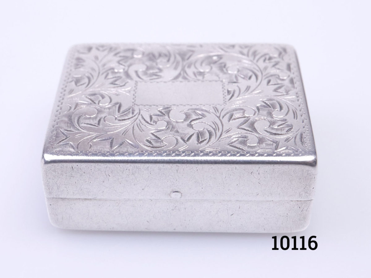 Vintage 950 grade silver pill/ snuff box. Hallmarked sterling 950 inside. Scrollwork to the lid with a vacant cartouche for personalisation. Close up photo of box seen from a slightly higher angle looking down and box front in the foreground