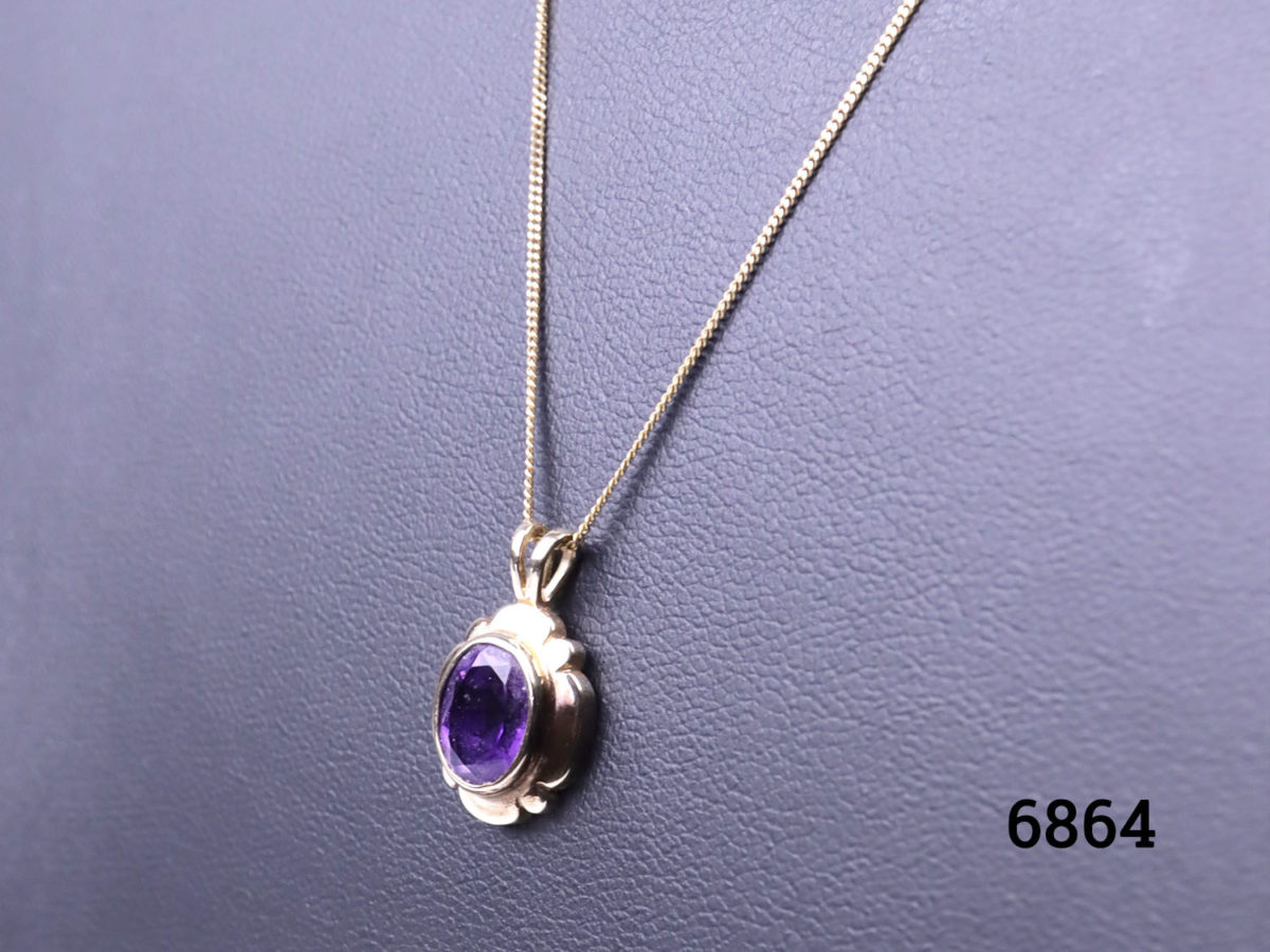 Vintage 9 karat gold fine necklace with a small 9 karat gold pendant set with oval cut amethyst stone. Pendant drop length 16mm Necklace chain length 500mm. Weight of chain and pendant 2.8 grams Close up photo of the pendant on a display stand and seen from a slight side angle