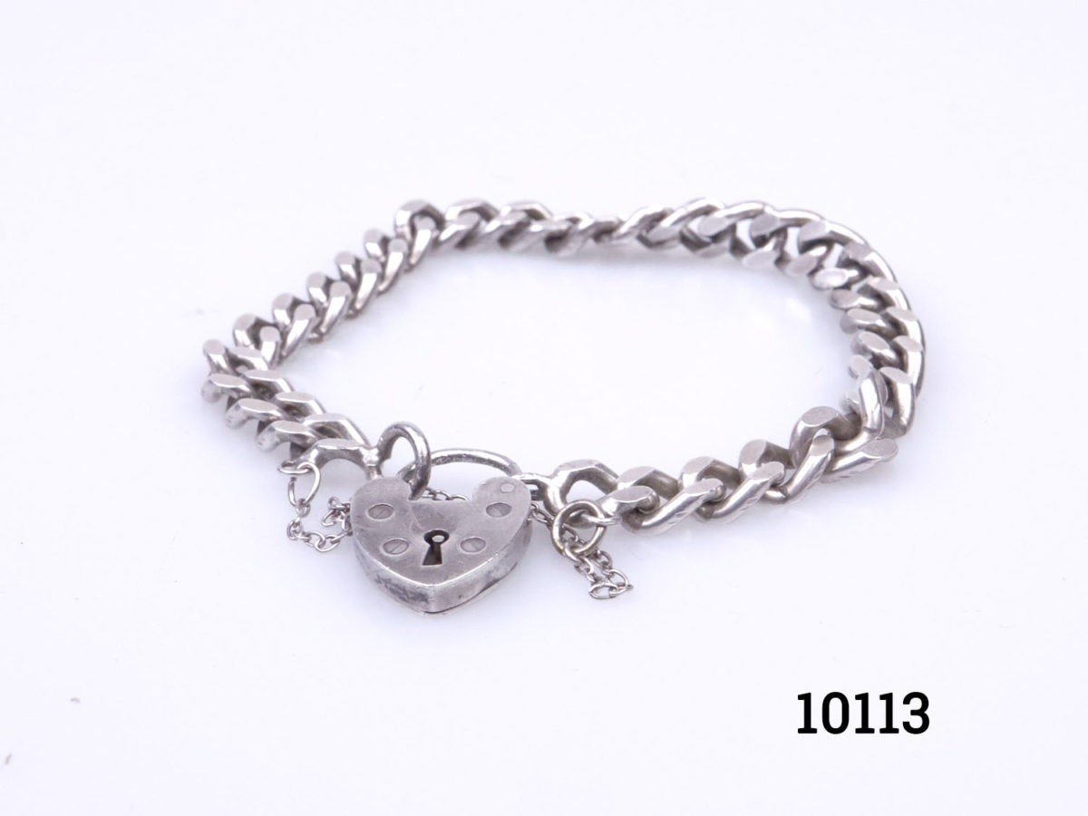 Vintage chunky sterling silver curb chain bracelet with heart shaped lock.Lion passant hallmark on one link and no hallmark on the lock. Safety chain extends opening. Lock has some signs of wear but fully functional. Photo of bracelet on a flat surface with heart lock in the foreground